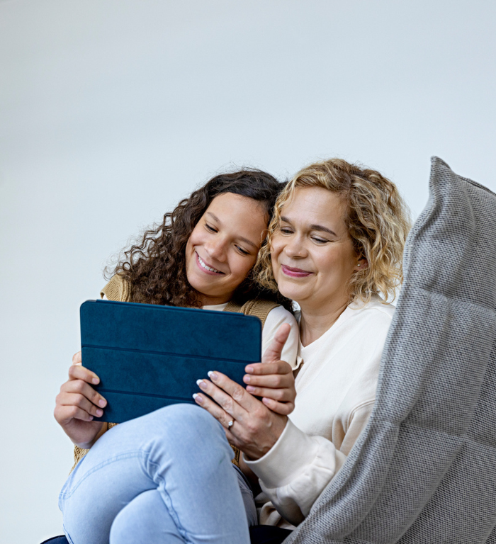 nainen ja tyttö istuvat nojatuolissa sylikkäin ja katsovat tablettia